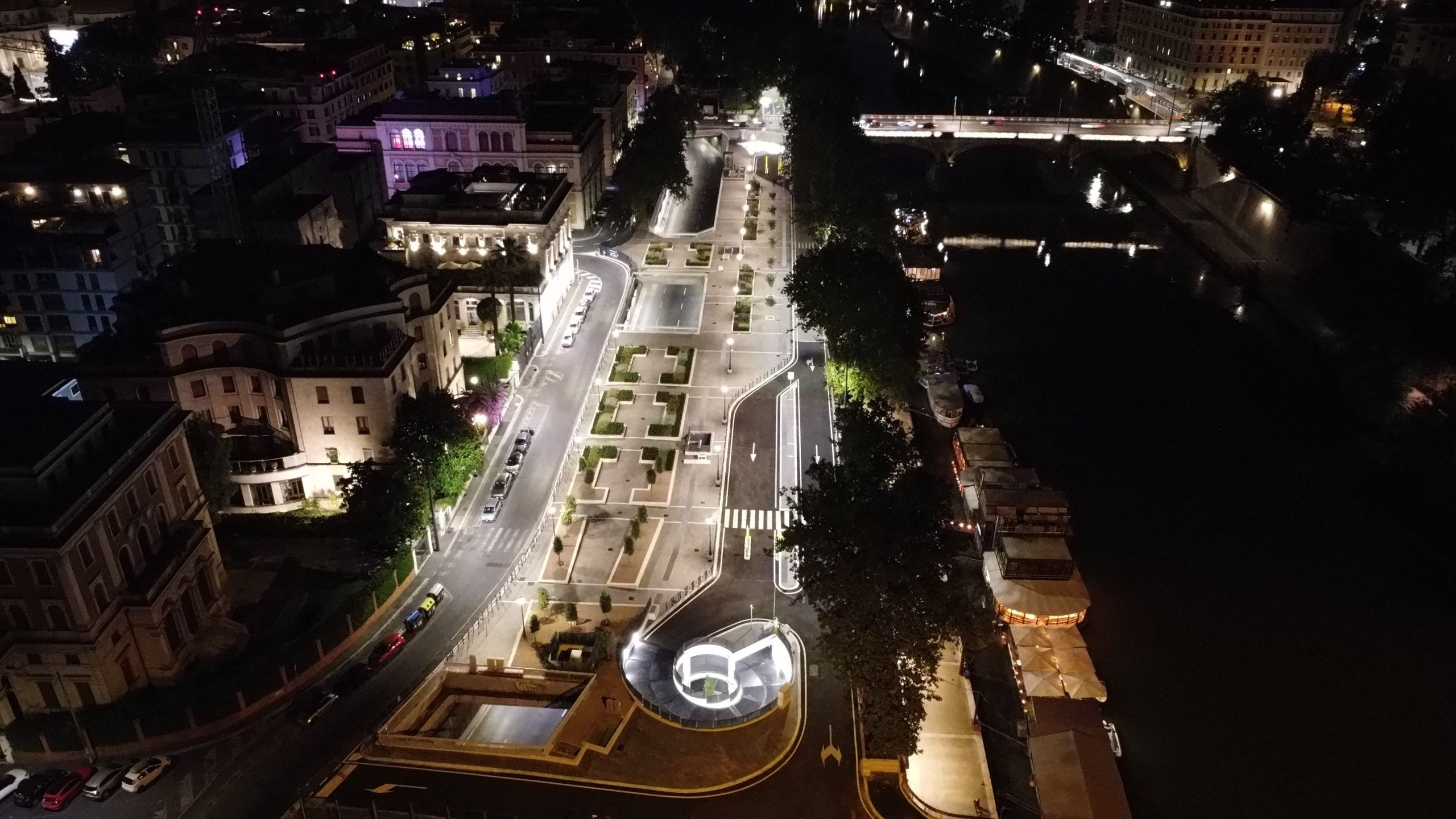 Piazza pedonale sopra il parcheggio illuminata di notte lungo il Tevere